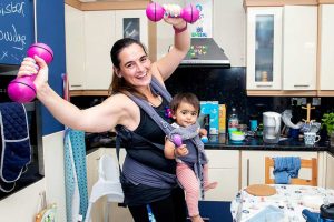 Alice1-774 Alice doing a home workout in her kitchen with her baby daughter in a sling.