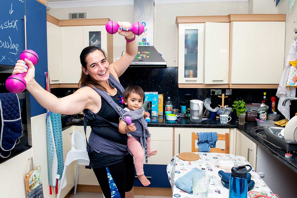 Alice doing a home workout in her kitchen with her baby daughter in a sling.